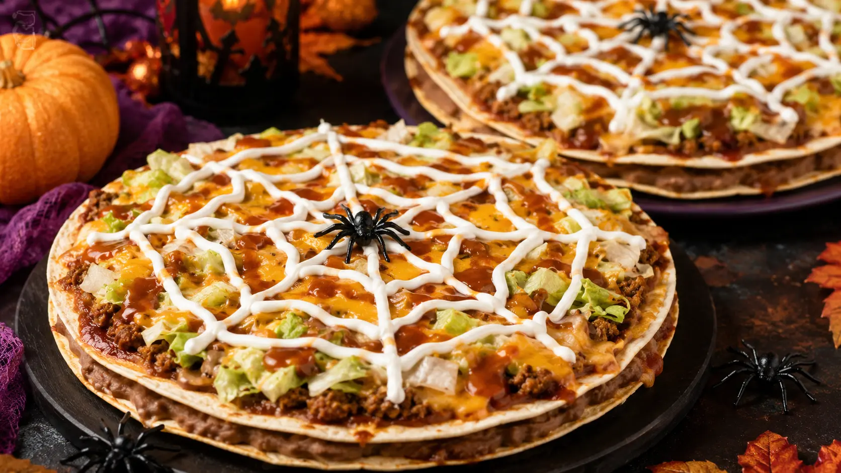 Easy spiderweb taco pizza for Halloween with crisp tortilla layers, taco-seasoned beef, cheddar, lettuce, enchilada sauce, and sour cream web